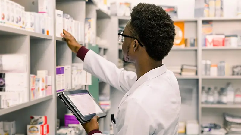 African American male pharmacist using digital tablet during inventory in pharmacy